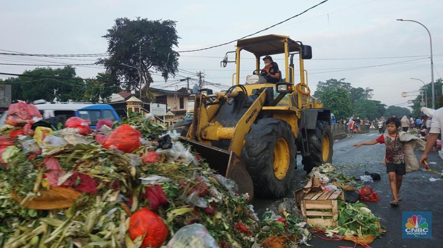 Seorang anak melintas di samping alat berat saat penanganan tumpukan sampah organik dan sisa makanan di kawasan Pasar Minggu, Jakarta, Jumat, (5/7/2024). (CNBC Indonesia/Muhammad Sabki)