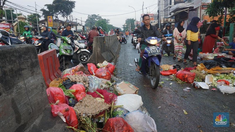 Seorang anak melintas di samping alat berat saat penanganan tumpukan sampah organik dan sisa makanan di kawasan Pasar Minggu, Jakarta, Jumat, (5/7/2024). (CNBC Indonesia/Muhammad Sabki)