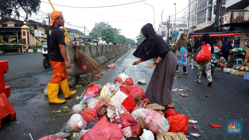 Seorang anak melintas di samping alat berat saat penanganan tumpukan sampah organik dan sisa makanan di kawasan Pasar Minggu, Jakarta, Jumat, (5/7/2024). (CNBC Indonesia/Muhammad Sabki)