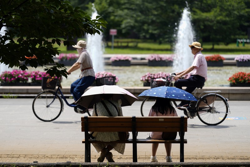 Orang-orang yang memegang payung duduk di bangku di bawah terik matahari di sebuah taman di Tokyo, Senin, 8 Juli 2024. Cuaca panas pada hari Senin telah terjadi dengan suhu meningkat lebih dari 35 derajat Celcius (95 derajat Fahrenheit) di Tokyo, menurut Jepang Badan Meteorologi. (AP Photo/Eugene Hoshiko)