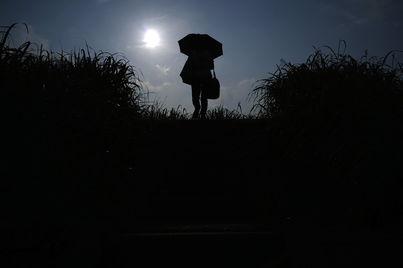 Orang-orang yang memegang payung duduk di bangku di bawah terik matahari di sebuah taman di Tokyo, Senin, 8 Juli 2024. Cuaca panas pada hari Senin telah terjadi dengan suhu meningkat lebih dari 35 derajat Celcius (95 derajat Fahrenheit) di Tokyo, menurut Jepang Badan Meteorologi. (AP Photo/Eugene Hoshiko)