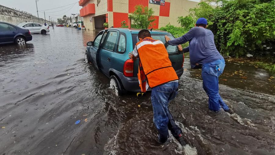 Pria mendorong mobil di jalan yang banjir saat hujan lebat di Veracruz, Meksiko 9 Juli 2024. (REUTERS/Stringer)