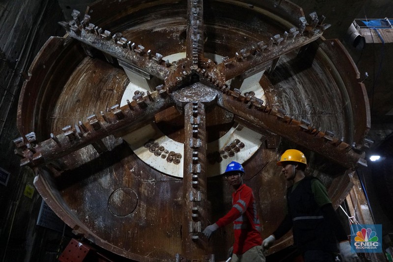 Sejumlah pekerja melintas di samping Tunnel Boring Machine (TBM) atau mesin bor bawah tanah di proyek MRT fase 2A Bundaran HI-Kota di kawasan Glodok, Jakarta, Kamis (11/7/2024). (CNBC Indonesia/Muhammad Sabki)