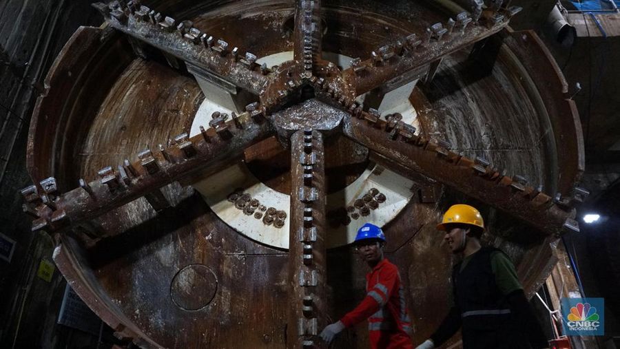 Sejumlah pekerja melintas di samping Tunnel Boring Machine (TBM) atau mesin bor bawah tanah di proyek MRT fase 2A Bundaran HI-Kota di kawasan Glodok, Jakarta, Kamis (11/7/2024). (CNBC Indonesia/Muhammad Sabki)