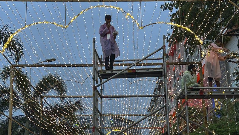 Orang-orang berjalan melewati tempat yang dihiasi lampu menjelang pernikahan putra miliarder Mukesh Ambani, Anant Ambani, dengan Radhika Merchant di Jio World Convention Center di Mumbai, India, Kamis, 11 Juli 2024. (AP Photo/Rafiq Maqbool)