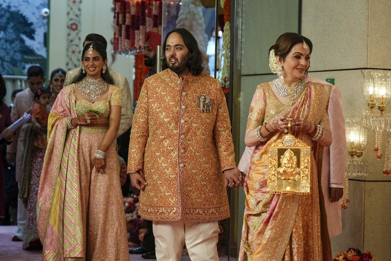 Miliarder Mukesh Ambani, tengah, menggandeng tangan putranya Anant Ambani saat mereka berjalan bersama Nita Ambani, kanan, di pernikahan Anant dan Radhika Merchant di Jio World Convention Center di Mumbai, India, Jumat, 12 Juli 2024. (AP Photo /Rajanish Kakade)