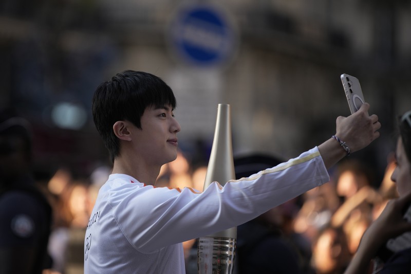 Jin, anggota tertua supergrup K-pop BTS, membawa obor Olimpiade, Minggu, 14 Juli 2024 di Paris. (AP Photo/Louise Delmotte)