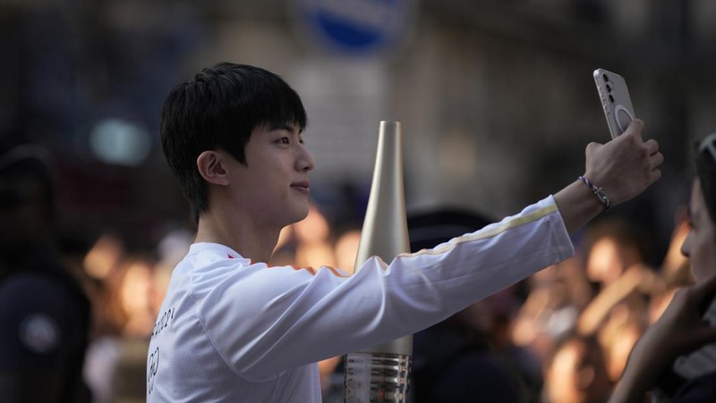 Jin, anggota tertua supergrup K-pop BTS, membawa obor Olimpiade, Minggu, 14 Juli 2024 di Paris. (AP Photo/Louise Delmotte)