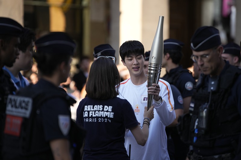 Jin, anggota tertua supergrup K-pop BTS, membawa obor Olimpiade, Minggu, 14 Juli 2024 di Paris. (AP Photo/Louise Delmotte)