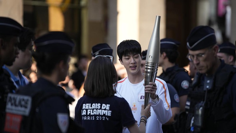 Jin, anggota tertua supergrup K-pop BTS, membawa obor Olimpiade, Minggu, 14 Juli 2024 di Paris. (AP Photo/Louise Delmotte)