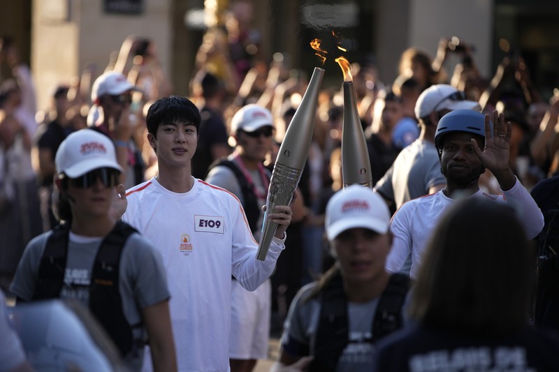 Jin, anggota tertua supergrup K-pop BTS, membawa obor Olimpiade, Minggu, 14 Juli 2024 di Paris. (AP Photo/Louise Delmotte)