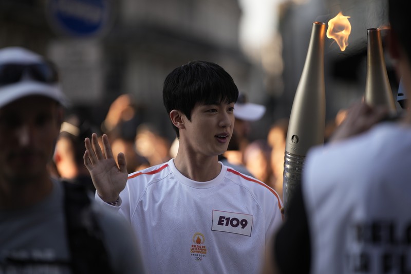 Jin, anggota tertua supergrup K-pop BTS, membawa obor Olimpiade, Minggu, 14 Juli 2024 di Paris. (AP Photo/Louise Delmotte)