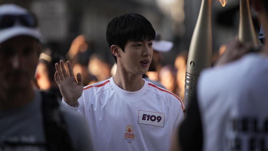 Jin, anggota tertua supergrup K-pop BTS, membawa obor Olimpiade, Minggu, 14 Juli 2024 di Paris. Jin akan membawa obor Olimpiade di area Museum Louvre Paris setelah baru saja menyelesaikan wajib militernya. (AP Photo/Louise Delmotte)