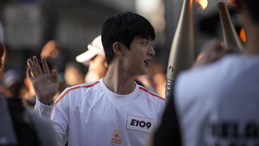 Jin, anggota tertua supergrup K-pop BTS, membawa obor Olimpiade, Minggu, 14 Juli 2024 di Paris. (AP Photo/Louise Delmotte)