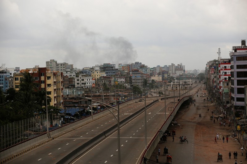 Petugas keamanan berjalan melewati kendaraan organisasi milik pemerintah yang rusak, yang dibakar oleh massa selama bentrokan setelah kekerasan meletus menyusul protes mahasiswa terhadap kuota pekerjaan pemerintah, di Dhaka, Bangladesh, 22 Juli 2024. (REUTERS/Mohammad Ponir Hossain)