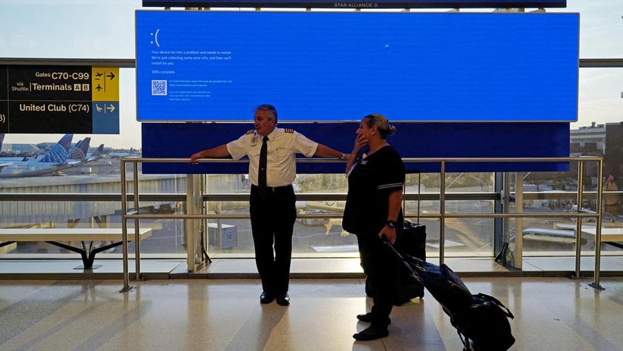 United Airlines employees wait by a departures monitor displaying a blue error screen, also known as the “Blue Screen of Death” inside Terminal C in Newark International Airport, after United Airlines and other airlines grounded flights due to a worldwide tech outage caused by an update to CrowdStrike's 