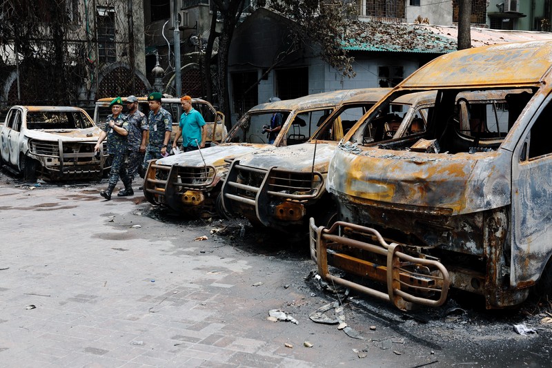 Petugas keamanan berjalan melewati kendaraan organisasi milik pemerintah yang rusak, yang dibakar oleh massa selama bentrokan setelah kekerasan meletus menyusul protes mahasiswa terhadap kuota pekerjaan pemerintah, di Dhaka, Bangladesh, 22 Juli 2024. Petugas keamanan berjalan melewati kendaraan organisasi milik pemerintah yang rusak, yang dibakar oleh massa selama bentrokan setelah kekerasan meletus menyusul protes mahasiswa terhadap kuota pekerjaan pemerintah, di Dhaka, Bangladesh, 22 Juli 2024. (REUTERS/Mohammad Ponir Hossain)