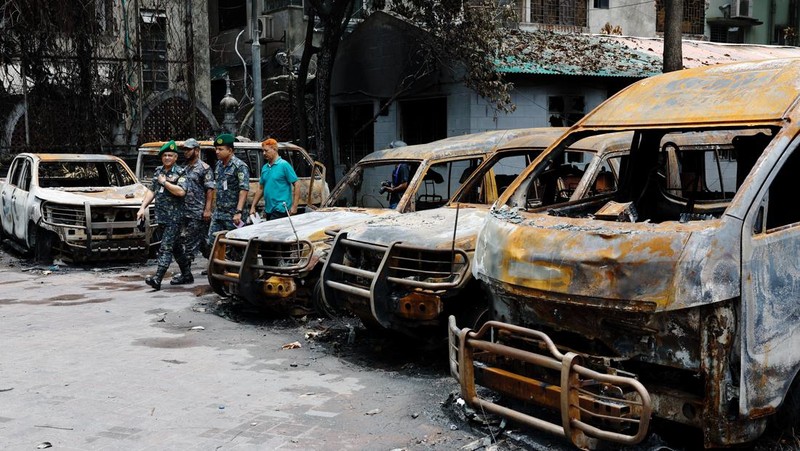 Petugas keamanan berjalan melewati kendaraan organisasi milik pemerintah yang rusak, yang dibakar oleh massa selama bentrokan setelah kekerasan meletus menyusul protes mahasiswa terhadap kuota pekerjaan pemerintah, di Dhaka, Bangladesh, 22 Juli 2024. (REUTERS/Mohammad Ponir Hossain)