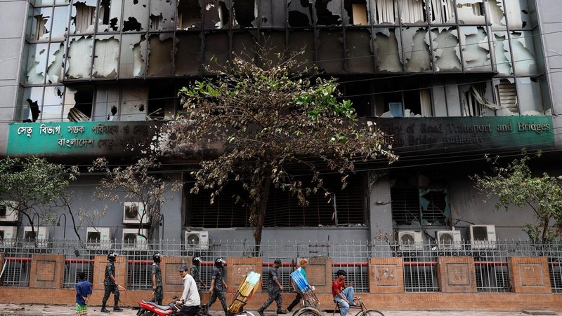 Petugas keamanan berjalan melewati kendaraan organisasi milik pemerintah yang rusak, yang dibakar oleh massa selama bentrokan setelah kekerasan meletus menyusul protes mahasiswa terhadap kuota pekerjaan pemerintah, di Dhaka, Bangladesh, 22 Juli 2024. (REUTERS/Mohammad Ponir Hossain)