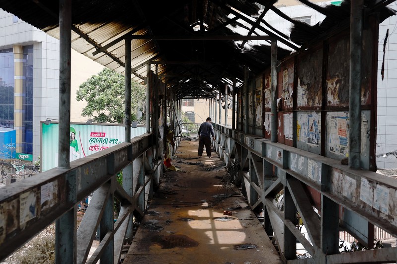 Petugas keamanan berjalan melewati kendaraan organisasi milik pemerintah yang rusak, yang dibakar oleh massa selama bentrokan setelah kekerasan meletus menyusul protes mahasiswa terhadap kuota pekerjaan pemerintah, di Dhaka, Bangladesh, 22 Juli 2024. Petugas keamanan berjalan melewati kendaraan organisasi milik pemerintah yang rusak, yang dibakar oleh massa selama bentrokan setelah kekerasan meletus menyusul protes mahasiswa terhadap kuota pekerjaan pemerintah, di Dhaka, Bangladesh, 22 Juli 2024. (REUTERS/Mohammad Ponir Hossain)