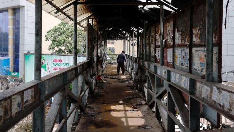 Petugas keamanan berjalan melewati kendaraan organisasi milik pemerintah yang rusak, yang dibakar oleh massa selama bentrokan setelah kekerasan meletus menyusul protes mahasiswa terhadap kuota pekerjaan pemerintah, di Dhaka, Bangladesh, 22 Juli 2024. (REUTERS/Mohammad Ponir Hossain)