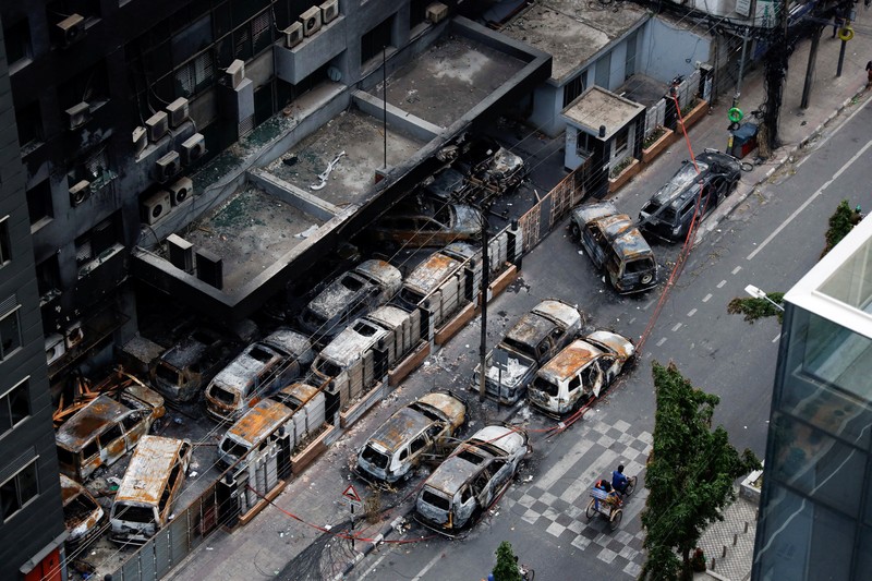 Petugas keamanan berjalan melewati kendaraan organisasi milik pemerintah yang rusak, yang dibakar oleh massa selama bentrokan setelah kekerasan meletus menyusul protes mahasiswa terhadap kuota pekerjaan pemerintah, di Dhaka, Bangladesh, 22 Juli 2024. Petugas keamanan berjalan melewati kendaraan organisasi milik pemerintah yang rusak, yang dibakar oleh massa selama bentrokan setelah kekerasan meletus menyusul protes mahasiswa terhadap kuota pekerjaan pemerintah, di Dhaka, Bangladesh, 22 Juli 2024. (REUTERS/Mohammad Ponir Hossain)