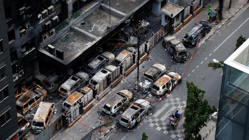 Petugas keamanan berjalan melewati kendaraan organisasi milik pemerintah yang rusak, yang dibakar oleh massa selama bentrokan setelah kekerasan meletus menyusul protes mahasiswa terhadap kuota pekerjaan pemerintah, di Dhaka, Bangladesh, 22 Juli 2024. (REUTERS/Mohammad Ponir Hossain)