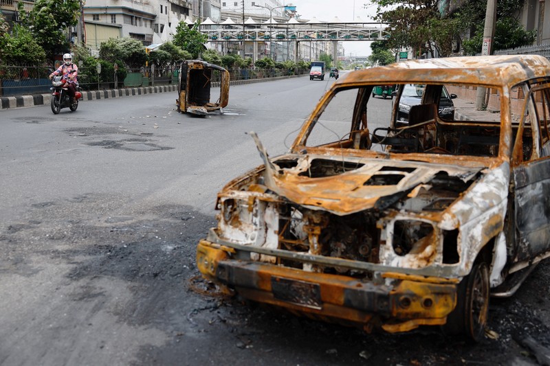 Petugas keamanan berjalan melewati kendaraan organisasi milik pemerintah yang rusak, yang dibakar oleh massa selama bentrokan setelah kekerasan meletus menyusul protes mahasiswa terhadap kuota pekerjaan pemerintah, di Dhaka, Bangladesh, 22 Juli 2024. Petugas keamanan berjalan melewati kendaraan organisasi milik pemerintah yang rusak, yang dibakar oleh massa selama bentrokan setelah kekerasan meletus menyusul protes mahasiswa terhadap kuota pekerjaan pemerintah, di Dhaka, Bangladesh, 22 Juli 2024. (REUTERS/Mohammad Ponir Hossain)
