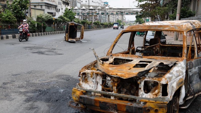 Petugas keamanan berjalan melewati kendaraan organisasi milik pemerintah yang rusak, yang dibakar oleh massa selama bentrokan setelah kekerasan meletus menyusul protes mahasiswa terhadap kuota pekerjaan pemerintah, di Dhaka, Bangladesh, 22 Juli 2024. (REUTERS/Mohammad Ponir Hossain)