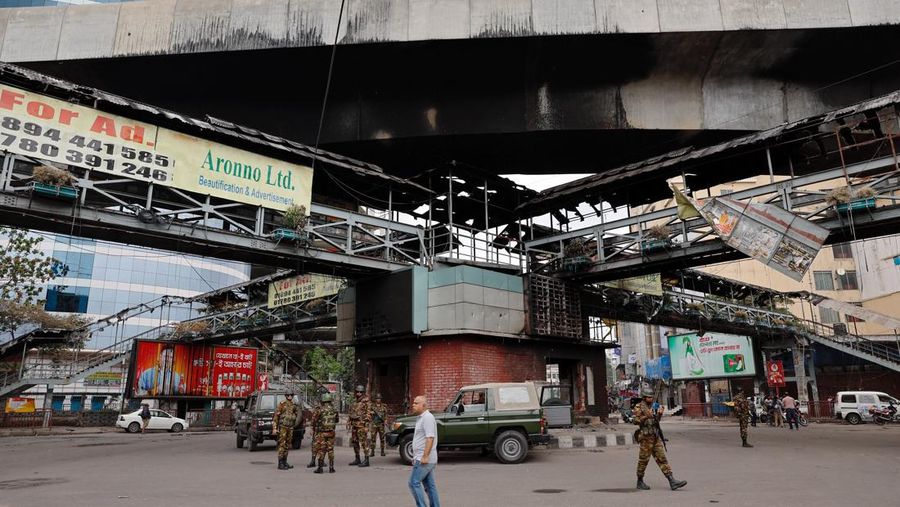 Petugas keamanan berjalan melewati kendaraan organisasi milik pemerintah yang rusak, yang dibakar oleh massa selama bentrokan setelah kekerasan meletus menyusul protes mahasiswa terhadap kuota pekerjaan pemerintah, di Dhaka, Bangladesh, 22 Juli 2024. (REUTERS/Mohammad Ponir Hossain)