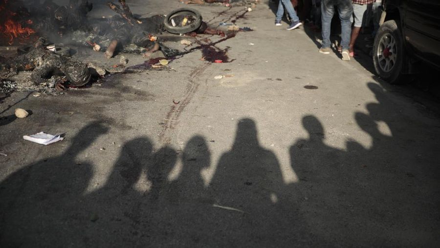 FILE - EDS NOTE: GRAPHIC CONTENT - Bystanders gather around the bodies of alleged gang members who were set on fire by a mob after they were stopped by police while traveling in a vehicle in the Canape Vert area of Port-au-Prince, Haiti, April 24, 2023. People are taking action and a wave of brutal vigilante justice is breaking across Haiti, closing off neighborhoods, stoning and often chopping the limbs of suspected gangsters, behead them and set them afire, sometimes while they are still alive. (AP Photo/Odelyn Joseph, File)