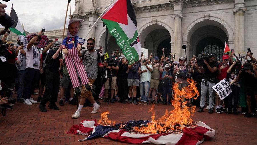 A U.S. flag burns as a pro-Palestinian demonstrator holds an effigy depicting Israeli Prime Minister Benjamin Netanyahu, outside Union Station, on the day of Netanyahu's address to a joint meeting of Congress on Capitol Hill, in Washington, U.S., July 24, 2024. REUTERS/Nathan Howard