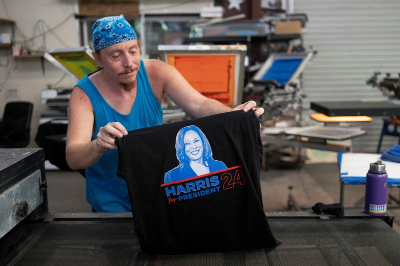 Juru cetak sablon Chris Fleury meletakkan kaus yang baru dicetak untuk mendukung kampanye kepresidenan Wakil Presiden AS Kamala Harris ke mesin pengering konveyor di Pabrik Gloo di Tucson, Arizona, AS, 25 Juli 2024. Juru cetak sablon Chris Fleury meletakkan kaus yang baru dicetak untuk mendukung kampanye kepresidenan Wakil Presiden AS Kamala Harris ke mesin pengering konveyor di Pabrik Gloo di Tucson, Arizona, AS, 25 Juli 2024. (REUTERS/Rebecca Noble)
