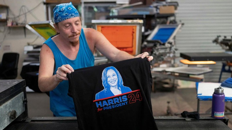 Juru cetak sablon Chris Fleury meletakkan kaus yang baru dicetak untuk mendukung kampanye kepresidenan Wakil Presiden AS Kamala Harris ke mesin pengering konveyor di Pabrik Gloo di Tucson, Arizona, AS, 25 Juli 2024. (REUTERS/Rebecca Noble)