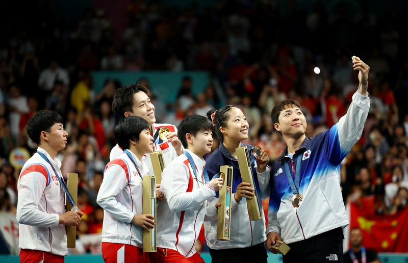 Paris 2024 Olympics - Table Tennis - Mixed Doubles Victory Ceremony - South Paris Arena 4, Paris, France - July 30, 2024. Bronze medallist Jonghoon Lim of South Korea takes selfie with Yubin Shin of South Korea and gold medallists Chuqin Wang of China and Yingsha Sun of China with silver medallists Jong Sik Ri of North Korea and Kum Yong Kim of North Korea on the podium with their medals after winning. REUTERS/Kim Hong-Ji