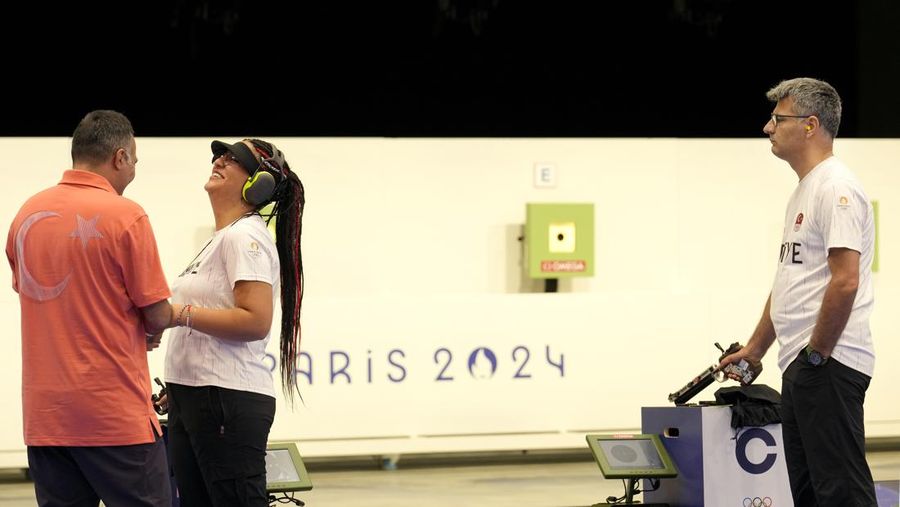 Turkish shooter Yusuf Dikec, right, looks on as Turkey's coach talks to Dikec's teammate Sevval Ilayda Tarhan during a time-out break at the 10m air pistol mixed team final, in Chateauroux, France, at the 2024 Summer Olympics, Tuesday, July 30, 2024. The Turkish team won the silver medal. (AP Photo/Manish Swarup)
