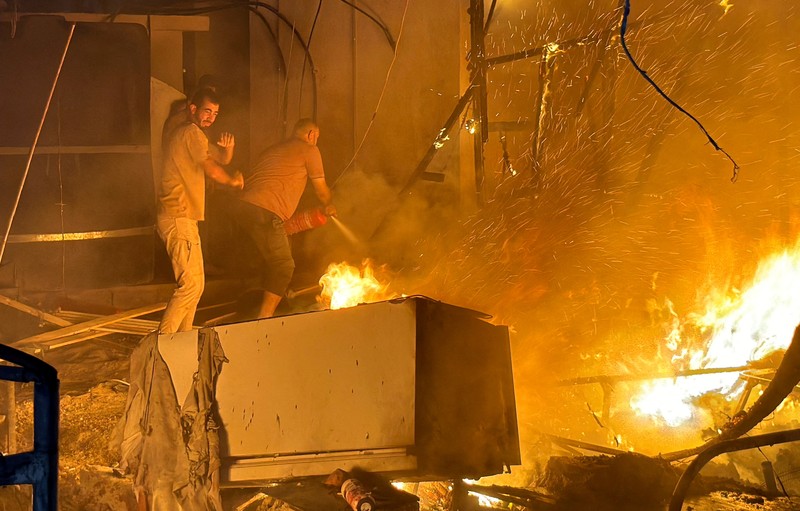 Warga Palestina bekerja memadamkan api di lokasi serangan Israel terhadap kamp tenda bagi para pengungsi, di tengah konflik Israel-Hamas, di Deir Al-Balah di Jalur Gaza tengah, 4 Agustus 2024. (REUTERS/Abdullah Al-Attar)