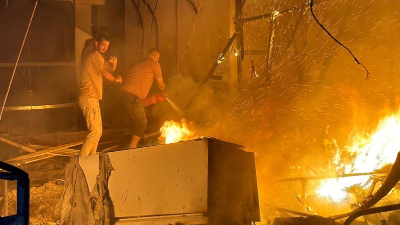 Warga Palestina bekerja memadamkan api di lokasi serangan Israel terhadap kamp tenda bagi para pengungsi, di tengah konflik Israel-Hamas, di Deir Al-Balah di Jalur Gaza tengah, 4 Agustus 2024. (REUTERS/Abdullah Al-Attar)