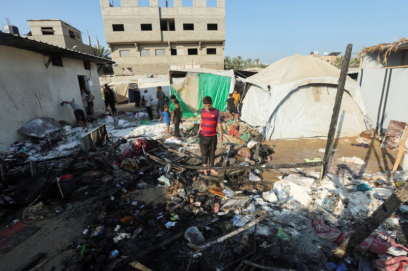 Warga Palestina bekerja memadamkan api di lokasi serangan Israel terhadap kamp tenda bagi para pengungsi, di tengah konflik Israel-Hamas, di Deir Al-Balah di Jalur Gaza tengah, 4 Agustus 2024. (REUTERS/Abdullah Al-Attar)