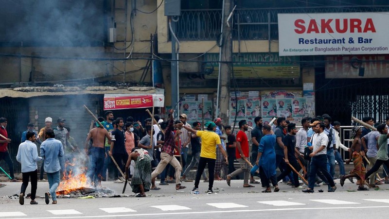 Pria berlari melewati pusat perbelanjaan yang dibakar oleh pengunjuk rasa selama unjuk rasa menentang Perdana Menteri Sheikh Hasina dan pemerintahannya yang menuntut keadilan bagi para korban yang tewas dalam bentrokan mematikan baru-baru ini di seluruh negeri, di Dhaka, Bangladesh, Minggu, 4 Agustus 2024. (AP Photo/Rajib Dhar)