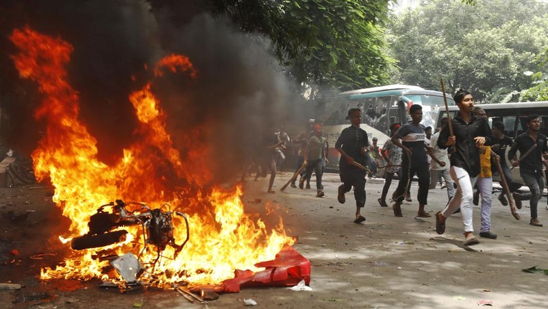 Pria berlari melewati pusat perbelanjaan yang dibakar oleh pengunjuk rasa selama unjuk rasa menentang Perdana Menteri Sheikh Hasina dan pemerintahannya yang menuntut keadilan bagi para korban yang tewas dalam bentrokan mematikan baru-baru ini di seluruh negeri, di Dhaka, Bangladesh, Minggu, 4 Agustus 2024. (AP Photo/Rajib Dhar)