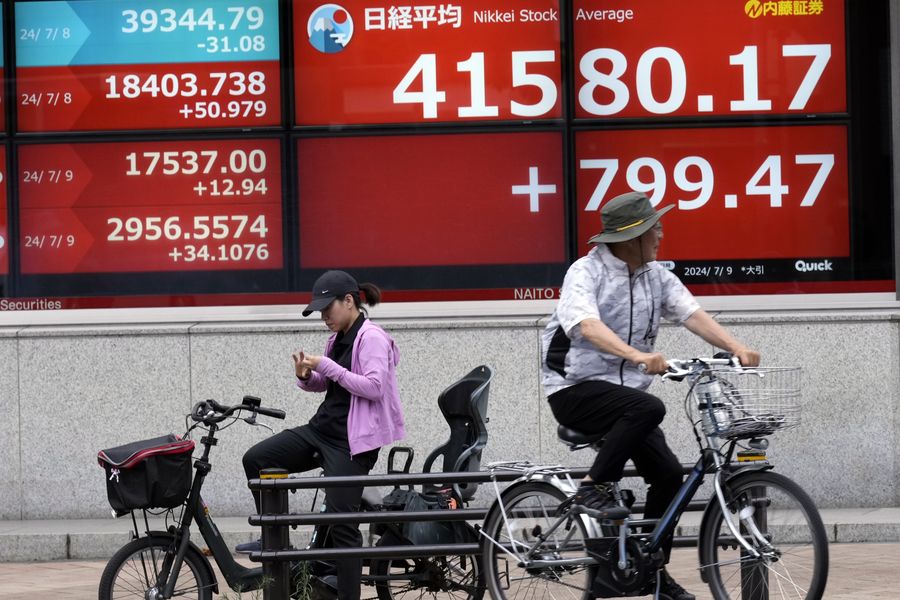 Orang-orang mengendarai sepeda di depan papan saham elektronik yang menunjukkan indeks Nikkei Jepang di sebuah perusahaan sekuritas pada hari Selasa, 9 Juli 2024, di Tokyo. Saham-saham Asia sebagian besar menguat pada hari Selasa setelah indeks acuan Wall Street mencapai lebih banyak tonggak sejarah. (AP/Eugene Hoshiko)