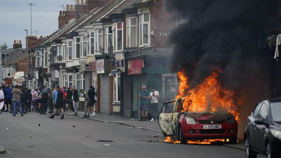 Sebuah mobil terbakar selama protes antiimigrasi di Middlesbrough, Inggris, Minggu 4 Agustus 2024. (Owen Humphreys/PA via AP)