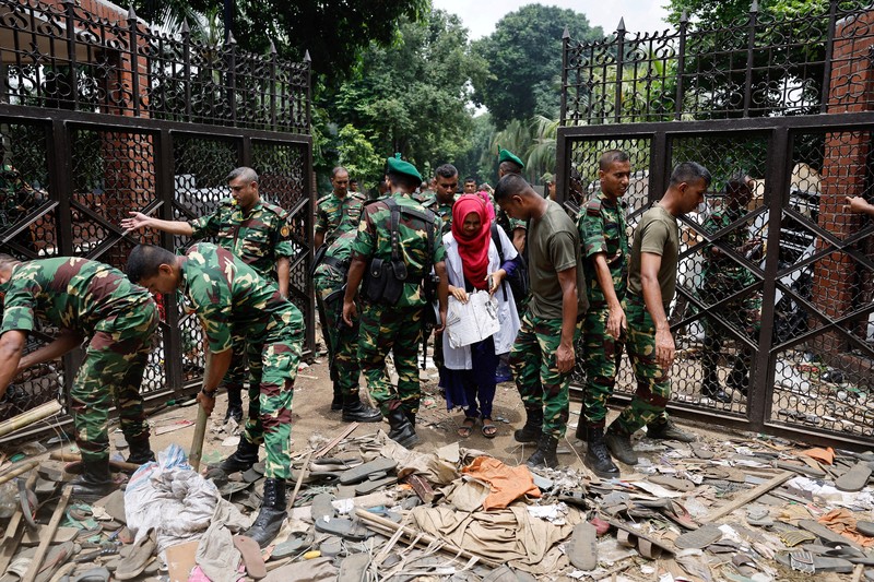 Para pengunjuk rasa antipemerintah berbaris menuju istana Perdana Menteri Sheikh Hasina sementara personel militer (tengah) berjaga di kawasan Shahbag, dekat Universitas Dhaka di Dhaka pada 5 Agustus 2024. Para pengunjuk rasa antipemerintah berbaris menuju istana Perdana Menteri Sheikh Hasina sementara personel militer (tengah) berjaga di kawasan Shahbag, dekat Universitas Dhaka di Dhaka pada 5 Agustus 2024. Protes di Bangladesh yang dimulai sebagai demonstrasi yang dipimpin mahasiswa terhadap aturan perekrutan pemerintah pada bulan Juli mencapai puncaknya pada tanggal 5 Agustus, saat perdana menteri melarikan diri dan militer mengumumkan akan membentuk pemerintahan sementara. (Photo by Munir UZ ZAMAN / AFP)