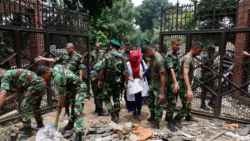 Para pengunjuk rasa antipemerintah berbaris menuju istana Perdana Menteri Sheikh Hasina sementara personel militer (tengah) berjaga di kawasan Shahbag, dekat Universitas Dhaka di Dhaka pada 5 Agustus 2024. Protes di Bangladesh yang dimulai sebagai demonstrasi yang dipimpin mahasiswa terhadap aturan perekrutan pemerintah pada bulan Juli mencapai puncaknya pada tanggal 5 Agustus, saat perdana menteri melarikan diri dan militer mengumumkan akan membentuk pemerintahan sementara. (Photo by Munir UZ ZAMAN / AFP)