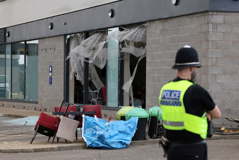 Seorang petugas polisi berjalan di luar hotel Holiday Inn Express setelah perusuh menyerang gedung tersebut di Rotherham, Inggris, 5 Agustus 2024. Pemerintah mengatakan gedung tersebut digunakan oleh pencari suaka. (REUTERS/Hollie Adams)