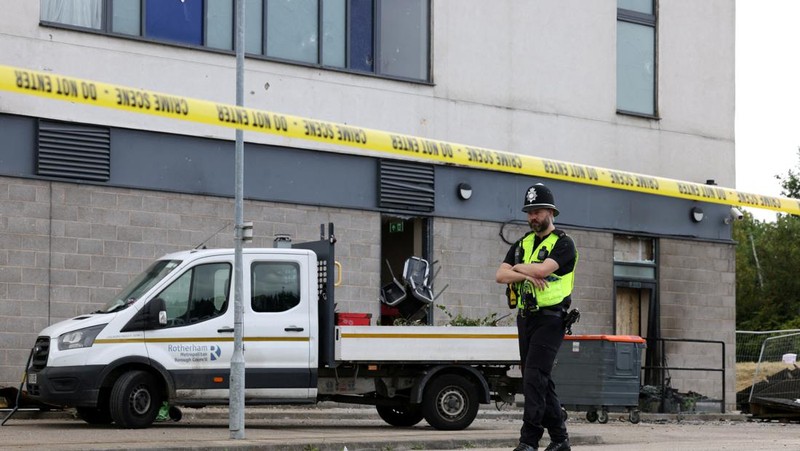 Seorang petugas polisi berjalan di luar hotel Holiday Inn Express setelah perusuh menyerang gedung tersebut di Rotherham, Inggris, 5 Agustus 2024. Pemerintah mengatakan gedung tersebut digunakan oleh pencari suaka. (REUTERS/Hollie Adams)