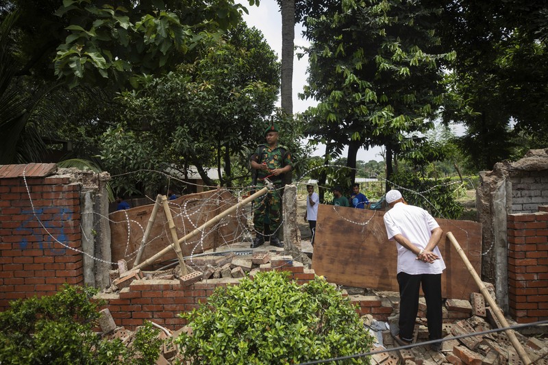 Para pengunjuk rasa antipemerintah berbaris menuju istana Perdana Menteri Sheikh Hasina sementara personel militer (tengah) berjaga di kawasan Shahbag, dekat Universitas Dhaka di Dhaka pada 5 Agustus 2024. Para pengunjuk rasa antipemerintah berbaris menuju istana Perdana Menteri Sheikh Hasina sementara personel militer (tengah) berjaga di kawasan Shahbag, dekat Universitas Dhaka di Dhaka pada 5 Agustus 2024. Protes di Bangladesh yang dimulai sebagai demonstrasi yang dipimpin mahasiswa terhadap aturan perekrutan pemerintah pada bulan Juli mencapai puncaknya pada tanggal 5 Agustus, saat perdana menteri melarikan diri dan militer mengumumkan akan membentuk pemerintahan sementara. (Photo by Munir UZ ZAMAN / AFP)