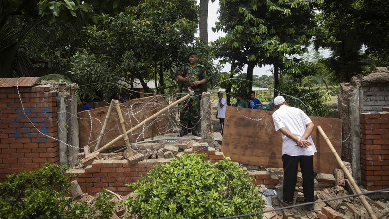 Para pengunjuk rasa antipemerintah berbaris menuju istana Perdana Menteri Sheikh Hasina sementara personel militer (tengah) berjaga di kawasan Shahbag, dekat Universitas Dhaka di Dhaka pada 5 Agustus 2024. Protes di Bangladesh yang dimulai sebagai demonstrasi yang dipimpin mahasiswa terhadap aturan perekrutan pemerintah pada bulan Juli mencapai puncaknya pada tanggal 5 Agustus, saat perdana menteri melarikan diri dan militer mengumumkan akan membentuk pemerintahan sementara. (Photo by Munir UZ ZAMAN / AFP)