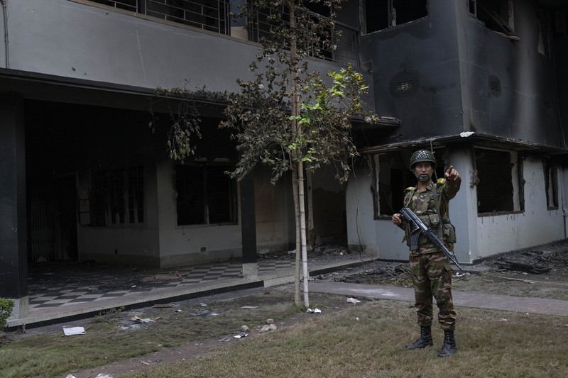 Para pengunjuk rasa antipemerintah berbaris menuju istana Perdana Menteri Sheikh Hasina sementara personel militer (tengah) berjaga di kawasan Shahbag, dekat Universitas Dhaka di Dhaka pada 5 Agustus 2024. Para pengunjuk rasa antipemerintah berbaris menuju istana Perdana Menteri Sheikh Hasina sementara personel militer (tengah) berjaga di kawasan Shahbag, dekat Universitas Dhaka di Dhaka pada 5 Agustus 2024. Protes di Bangladesh yang dimulai sebagai demonstrasi yang dipimpin mahasiswa terhadap aturan perekrutan pemerintah pada bulan Juli mencapai puncaknya pada tanggal 5 Agustus, saat perdana menteri melarikan diri dan militer mengumumkan akan membentuk pemerintahan sementara. (Photo by Munir UZ ZAMAN / AFP)